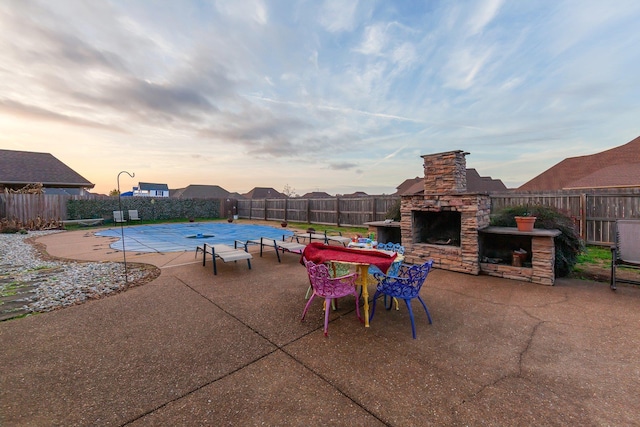 patio terrace at dusk featuring an outdoor stone fireplace and a covered pool