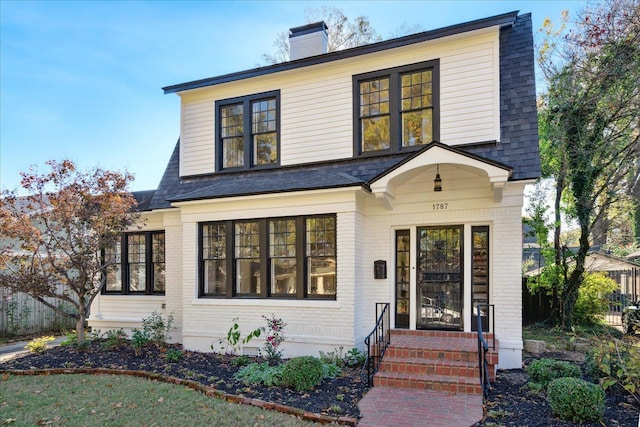 view of front of home with brick siding, a chimney, roof with shingles, and fence