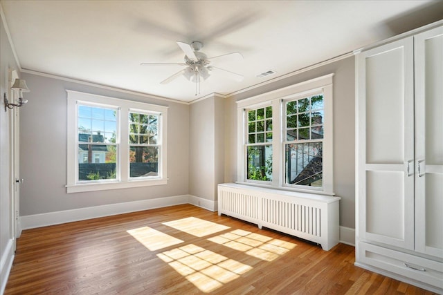 empty room with radiator, plenty of natural light, light hardwood / wood-style floors, and ornamental molding