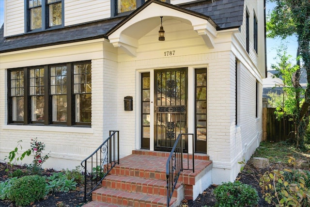 entrance to property featuring fence, brick siding, and a shingled roof