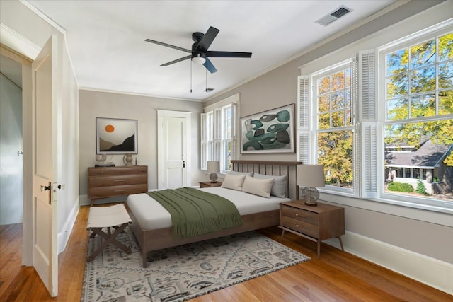bedroom featuring visible vents, a ceiling fan, wood finished floors, crown molding, and baseboards