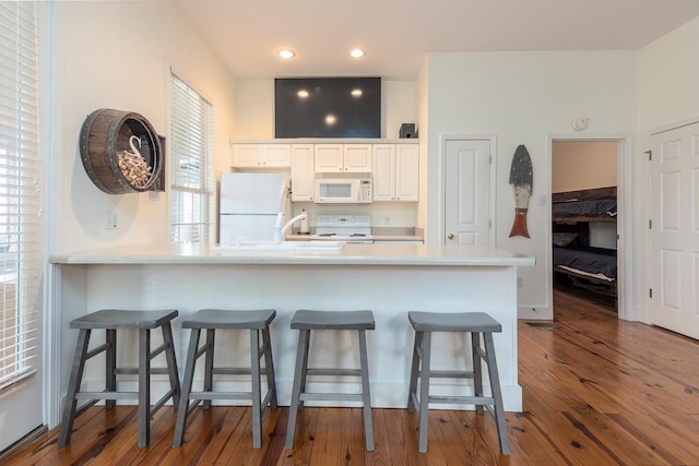 kitchen featuring a kitchen bar, white appliances, white cabinetry, and dark wood-type flooring