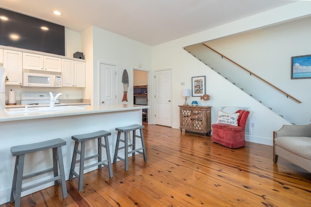 kitchen with kitchen peninsula, hardwood / wood-style floors, white appliances, a breakfast bar area, and white cabinets