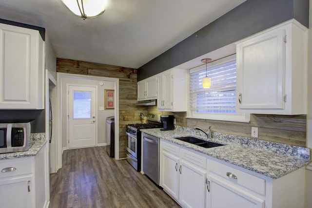 kitchen featuring a healthy amount of sunlight, wooden walls, sink, white cabinets, and hanging light fixtures