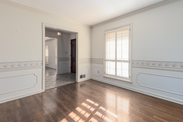 spare room with dark wood-type flooring, wainscoting, visible vents, and crown molding