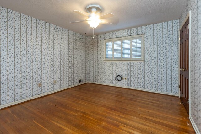 spare room with a textured ceiling, wood finished floors, and wallpapered walls