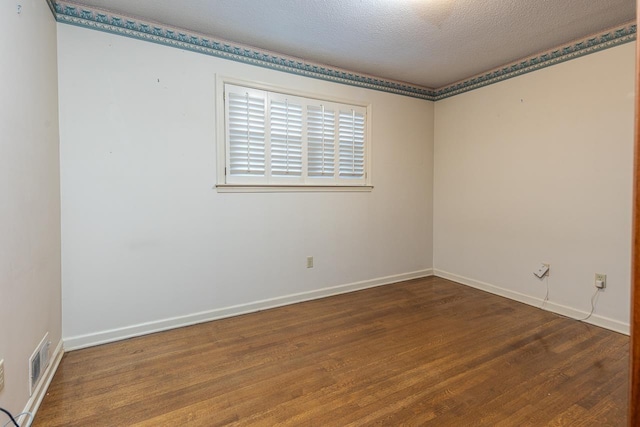 empty room with visible vents, a textured ceiling, baseboards, and wood finished floors