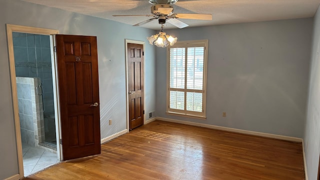 unfurnished bedroom featuring a chandelier, wood finished floors, connected bathroom, and baseboards