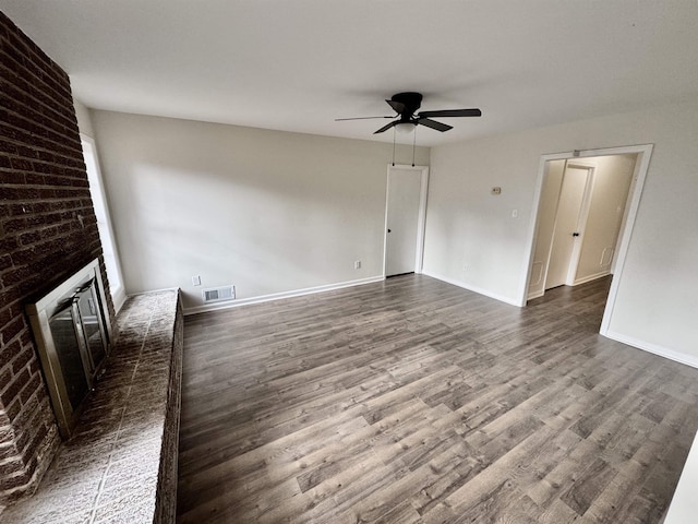 empty room with ceiling fan, a fireplace, and dark wood-type flooring