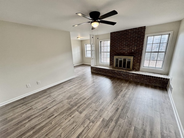 unfurnished living room with ceiling fan, dark wood-type flooring, a wealth of natural light, and a brick fireplace