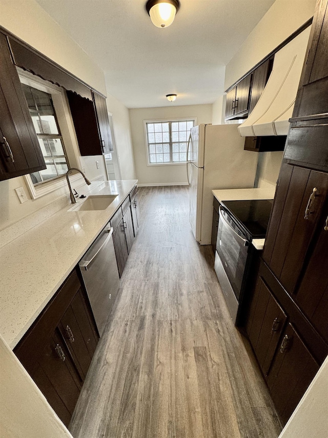 kitchen featuring sink, light stone countertops, light wood-type flooring, appliances with stainless steel finishes, and dark brown cabinetry