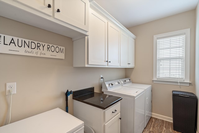 clothes washing area with washing machine and clothes dryer, dark wood-type flooring, and cabinets