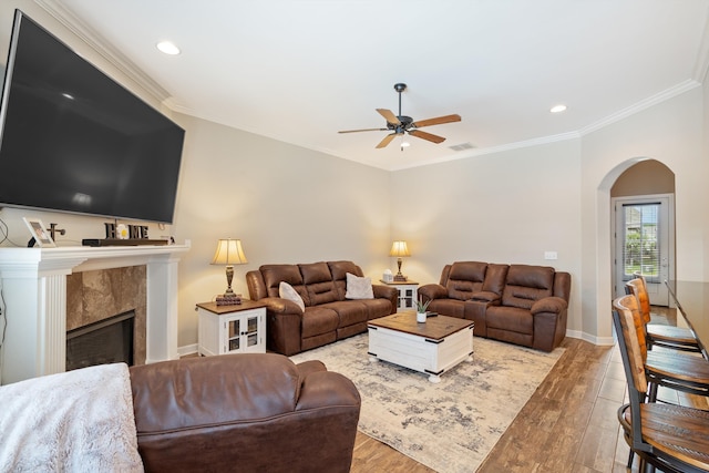 living room with a tile fireplace, crown molding, ceiling fan, and light hardwood / wood-style floors