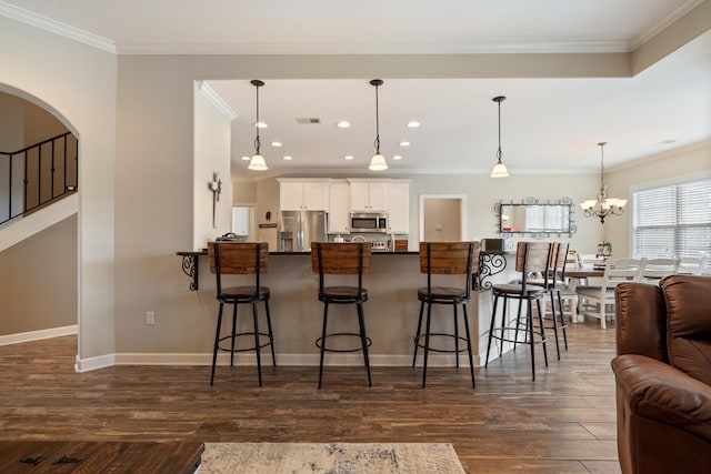 kitchen featuring white cabinetry, hanging light fixtures, crown molding, a kitchen bar, and appliances with stainless steel finishes