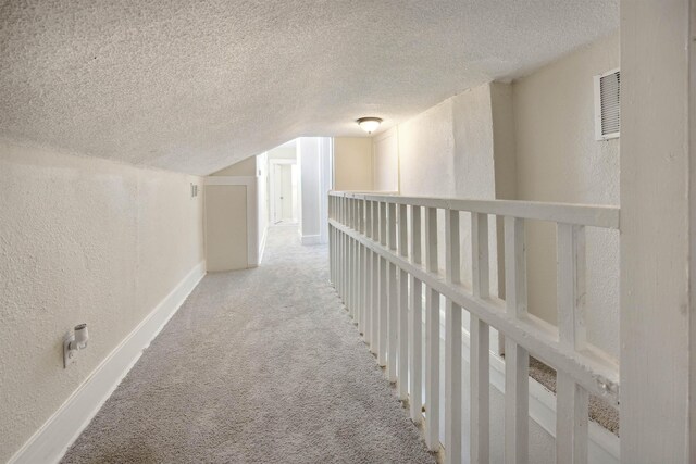 corridor with carpet flooring, vaulted ceiling, and a textured ceiling