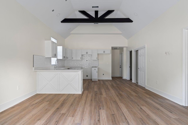 kitchen with kitchen peninsula, hardwood / wood-style flooring, high vaulted ceiling, and tasteful backsplash