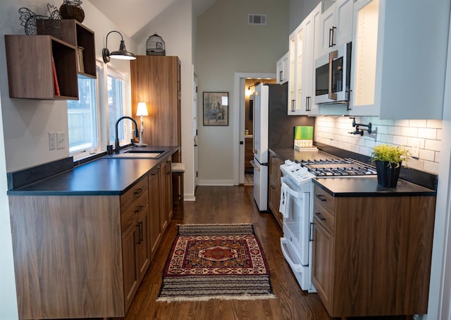 kitchen featuring white gas range, sink, dark hardwood / wood-style floors, vaulted ceiling, and decorative backsplash