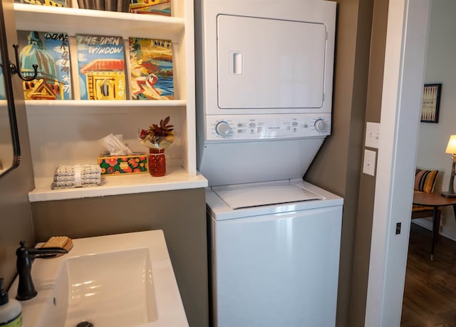 clothes washing area with dark hardwood / wood-style flooring, stacked washing maching and dryer, and sink