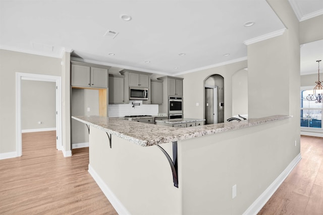 kitchen featuring tasteful backsplash, light hardwood / wood-style flooring, kitchen peninsula, a breakfast bar area, and appliances with stainless steel finishes