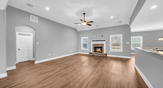 unfurnished living room featuring hardwood / wood-style flooring, ceiling fan, a stone fireplace, and vaulted ceiling