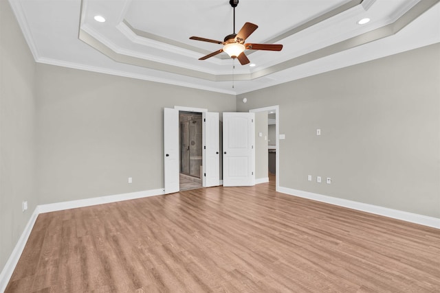 unfurnished bedroom featuring a raised ceiling, crown molding, ceiling fan, a spacious closet, and light wood-type flooring