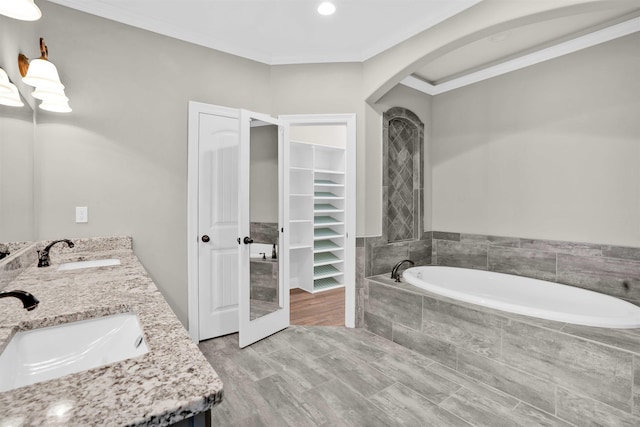 bathroom with tiled tub, vanity, wood-type flooring, and ornamental molding