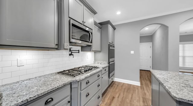 kitchen with gray cabinetry, crown molding, light hardwood / wood-style flooring, and stainless steel appliances