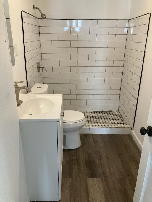 bathroom featuring toilet, vanity, wood-type flooring, and tiled shower