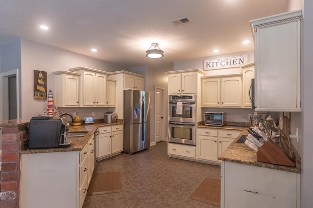 kitchen featuring dark stone counters, kitchen peninsula, sink, and stainless steel appliances