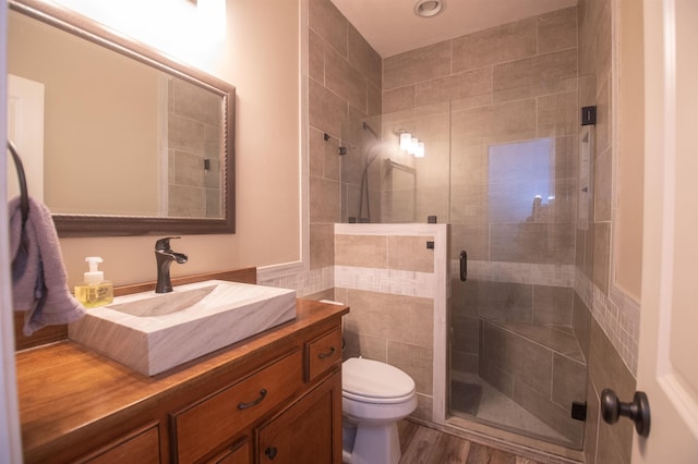 bathroom with vanity, hardwood / wood-style flooring, toilet, tile walls, and a shower with shower door