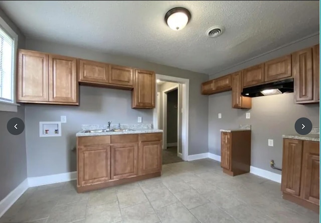 kitchen featuring a textured ceiling, light stone countertops, and sink