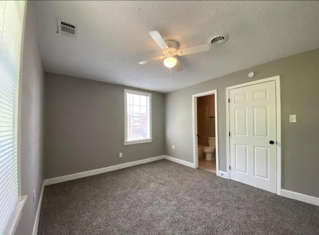 unfurnished bedroom with dark colored carpet, a textured ceiling, ensuite bath, and ceiling fan