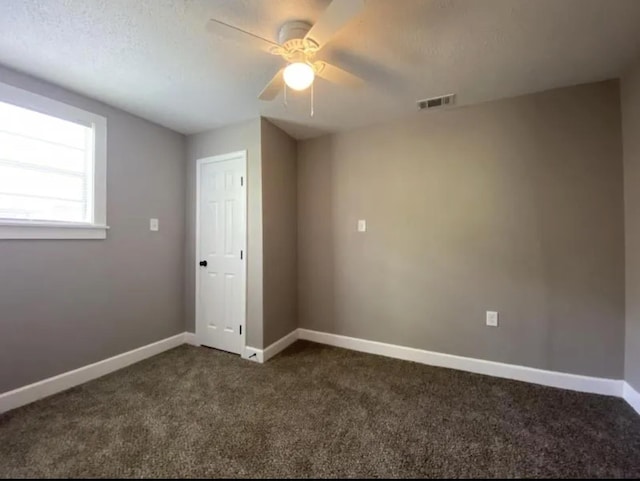 spare room with ceiling fan, a textured ceiling, and dark colored carpet