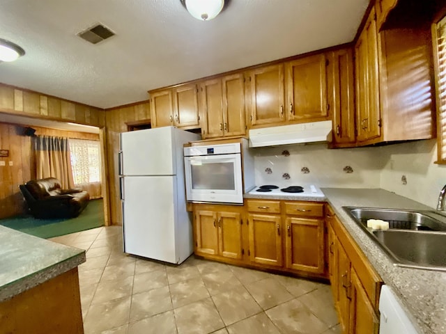 kitchen featuring sink, a textured ceiling, white appliances, wooden walls, and light tile patterned floors