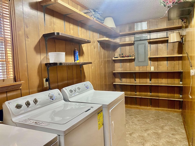 laundry room with washer and dryer, electric panel, a textured ceiling, and wooden walls