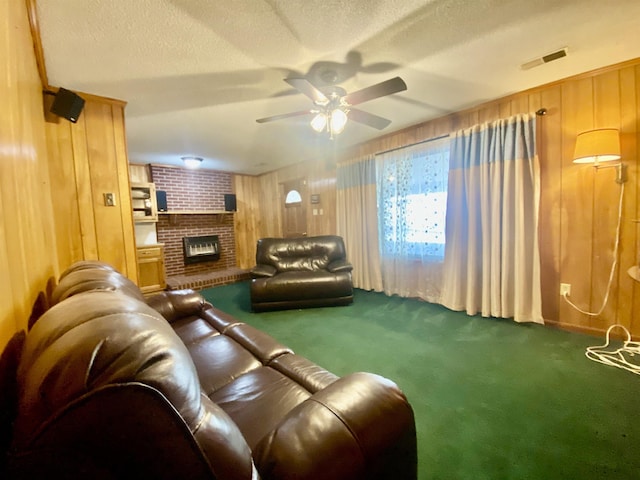 carpeted living room with a fireplace, a textured ceiling, ceiling fan, and wooden walls