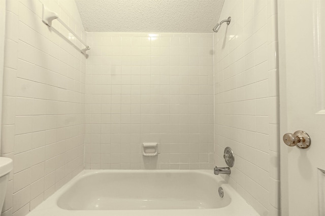 bathroom featuring tiled shower / bath, toilet, and a textured ceiling