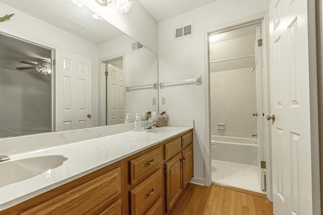 bathroom with a textured ceiling, vanity, tiled shower / bath combo, hardwood / wood-style flooring, and ceiling fan