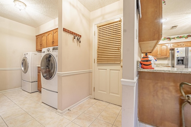 clothes washing area featuring light tile patterned flooring, cabinets, separate washer and dryer, and a textured ceiling