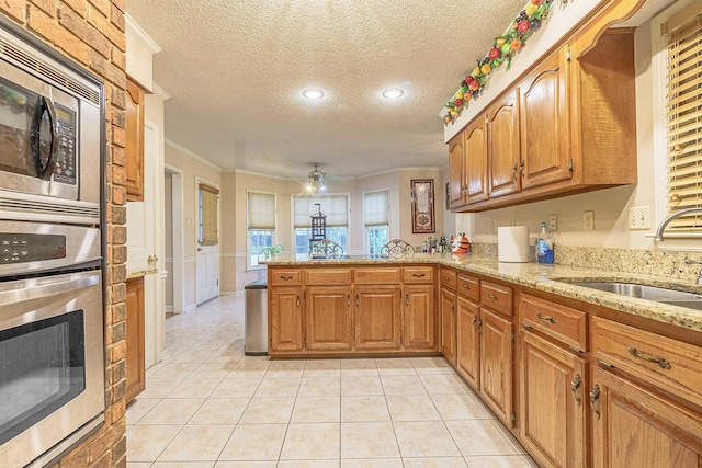 kitchen featuring sink, a textured ceiling, ornamental molding, kitchen peninsula, and stainless steel appliances