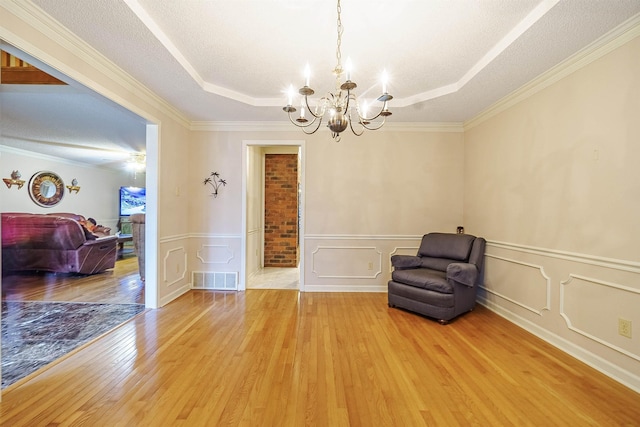 living area featuring hardwood / wood-style flooring, ornamental molding, a raised ceiling, and a textured ceiling