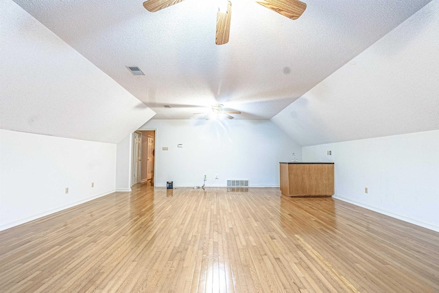 additional living space featuring lofted ceiling, a textured ceiling, light hardwood / wood-style floors, and ceiling fan