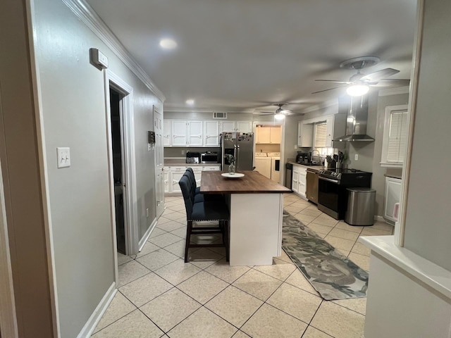 kitchen with white cabinetry, a center island, wall chimney exhaust hood, wood counters, and appliances with stainless steel finishes