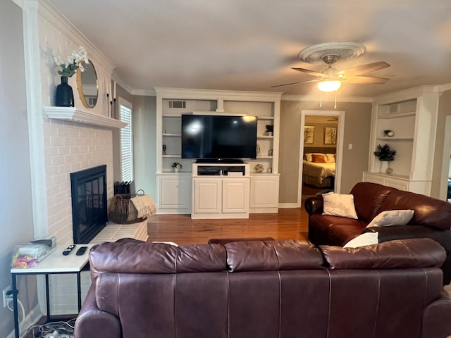 living room featuring hardwood / wood-style floors, ceiling fan, built in shelves, ornamental molding, and a fireplace