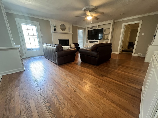 living room featuring ceiling fan, ornamental molding, wood-type flooring, and a brick fireplace