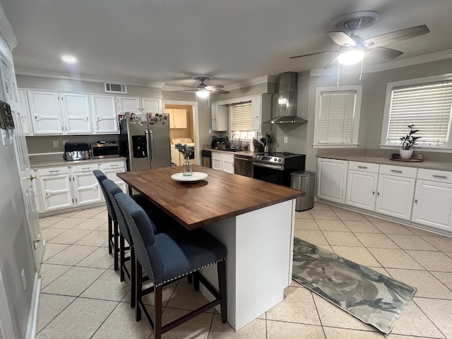 kitchen featuring wood counters, appliances with stainless steel finishes, wall chimney exhaust hood, white cabinetry, and a kitchen island