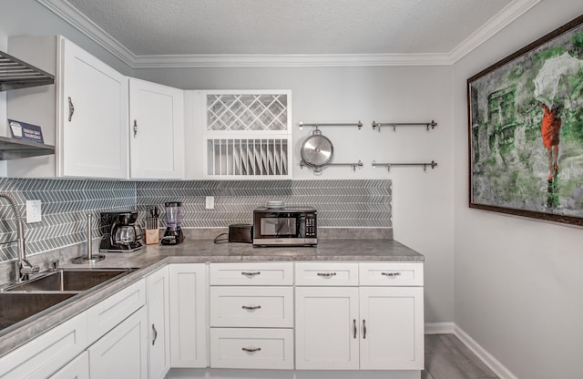 kitchen featuring backsplash, ornamental molding, a textured ceiling, sink, and white cabinets