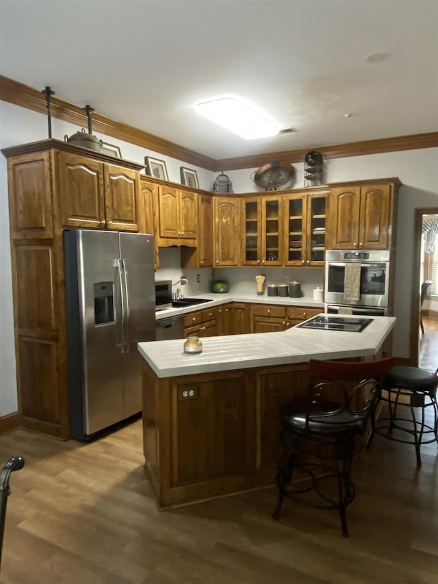 kitchen with a breakfast bar area, ornamental molding, stainless steel appliances, and light hardwood / wood-style floors