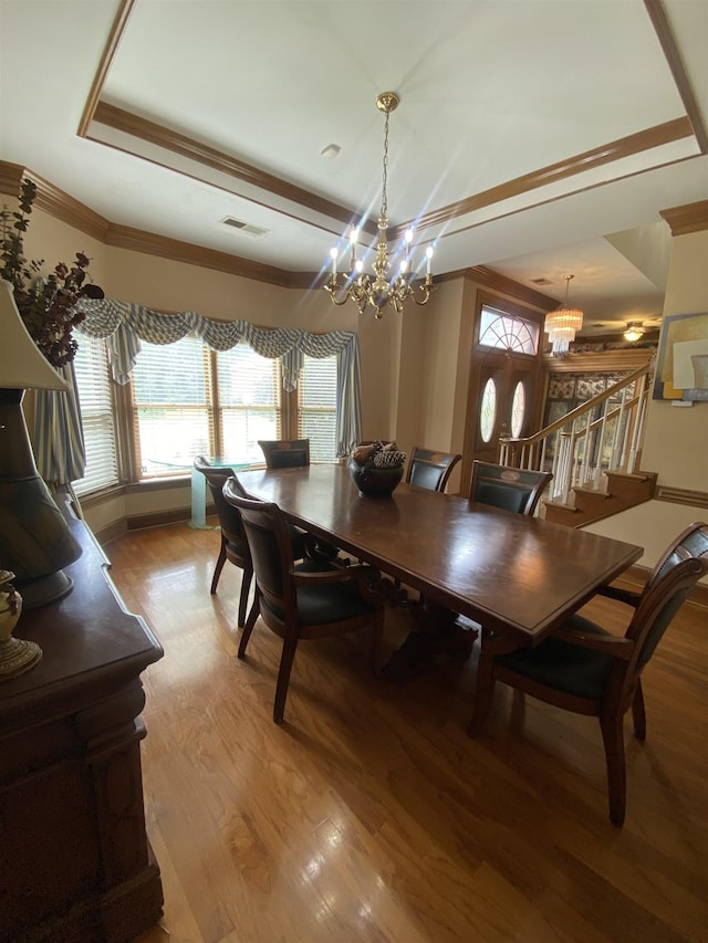 dining area featuring a chandelier, light hardwood / wood-style floors, a tray ceiling, and crown molding