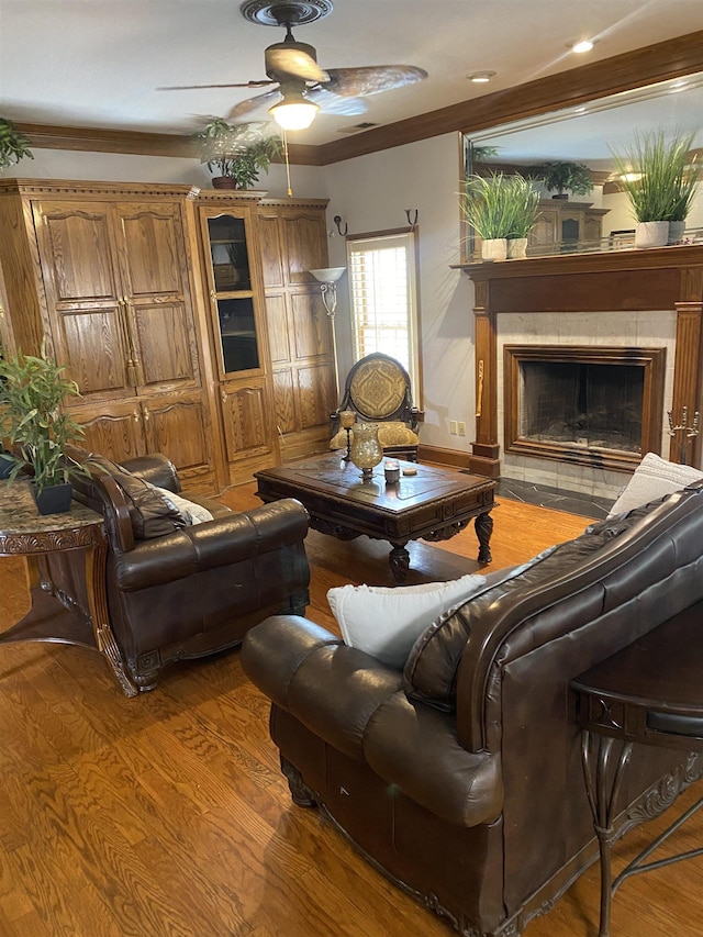 living room featuring hardwood / wood-style flooring, ceiling fan, crown molding, and a tiled fireplace